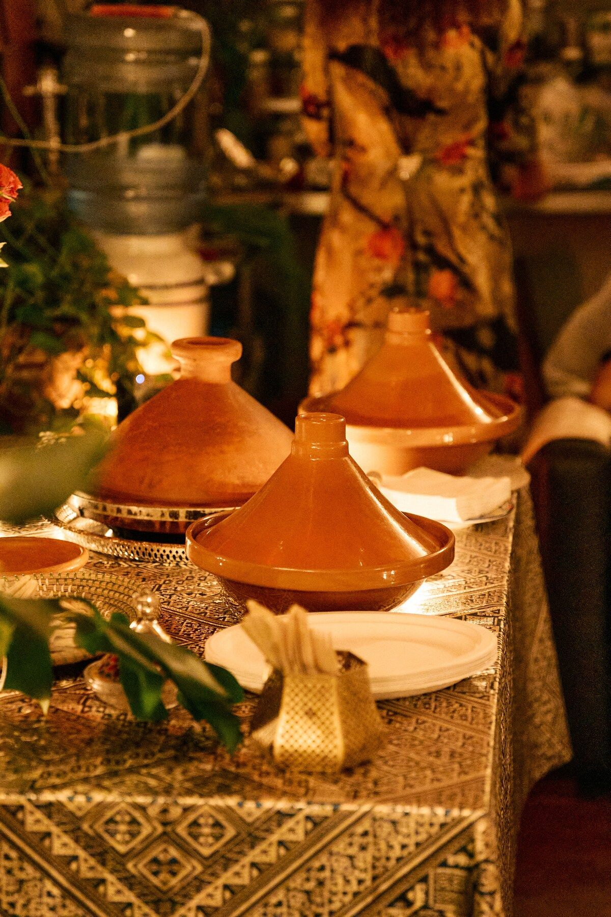Clay tagines on a patterned Moroccan tablecloth, lit by candles.