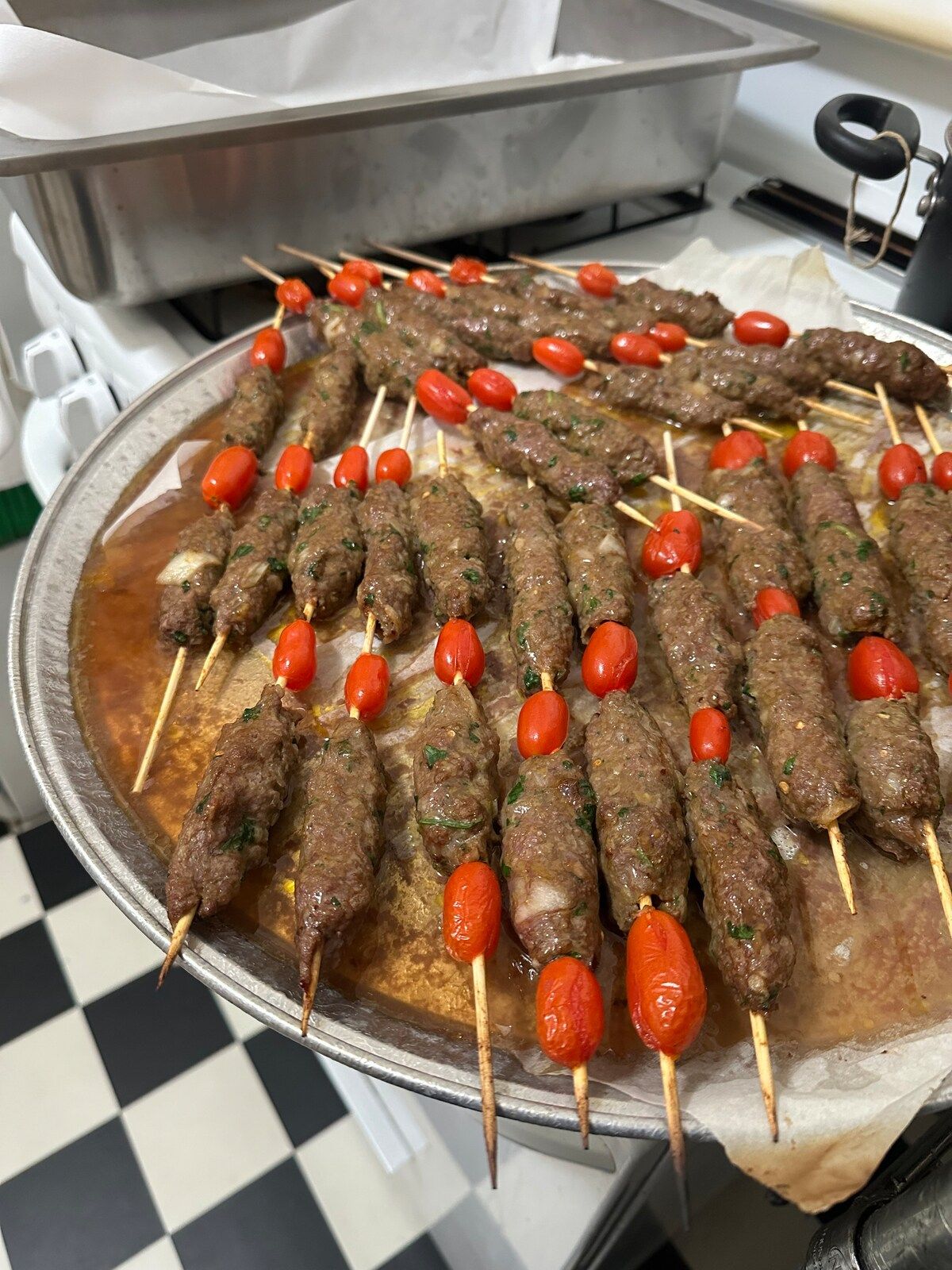 Grilled beef kefta skewers with cherry tomatoes on a large silver tray.