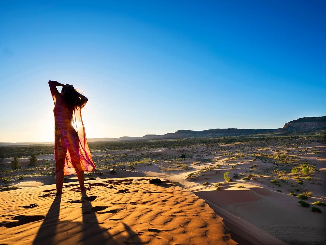 Chef Basmah standing on a sand dune against a clear blue sky.