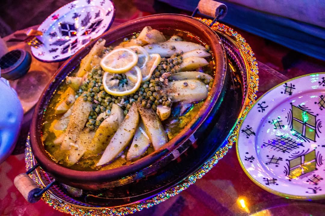 A fish tagine with lemon slices, peas and herbs next to hand-painted plates.