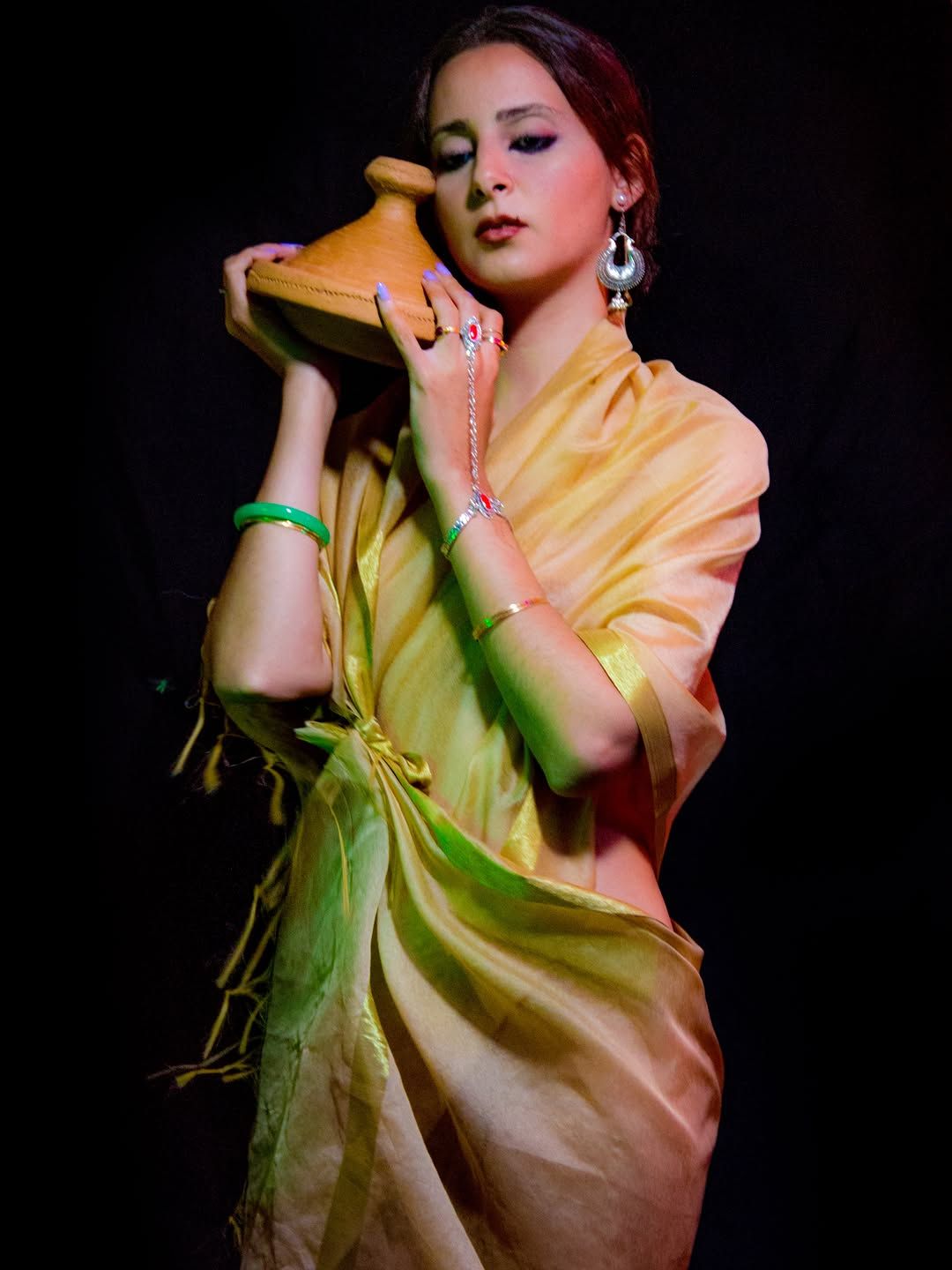 Chef Basmah in a golden silk wrap holding a clay tagine at her shoulder.