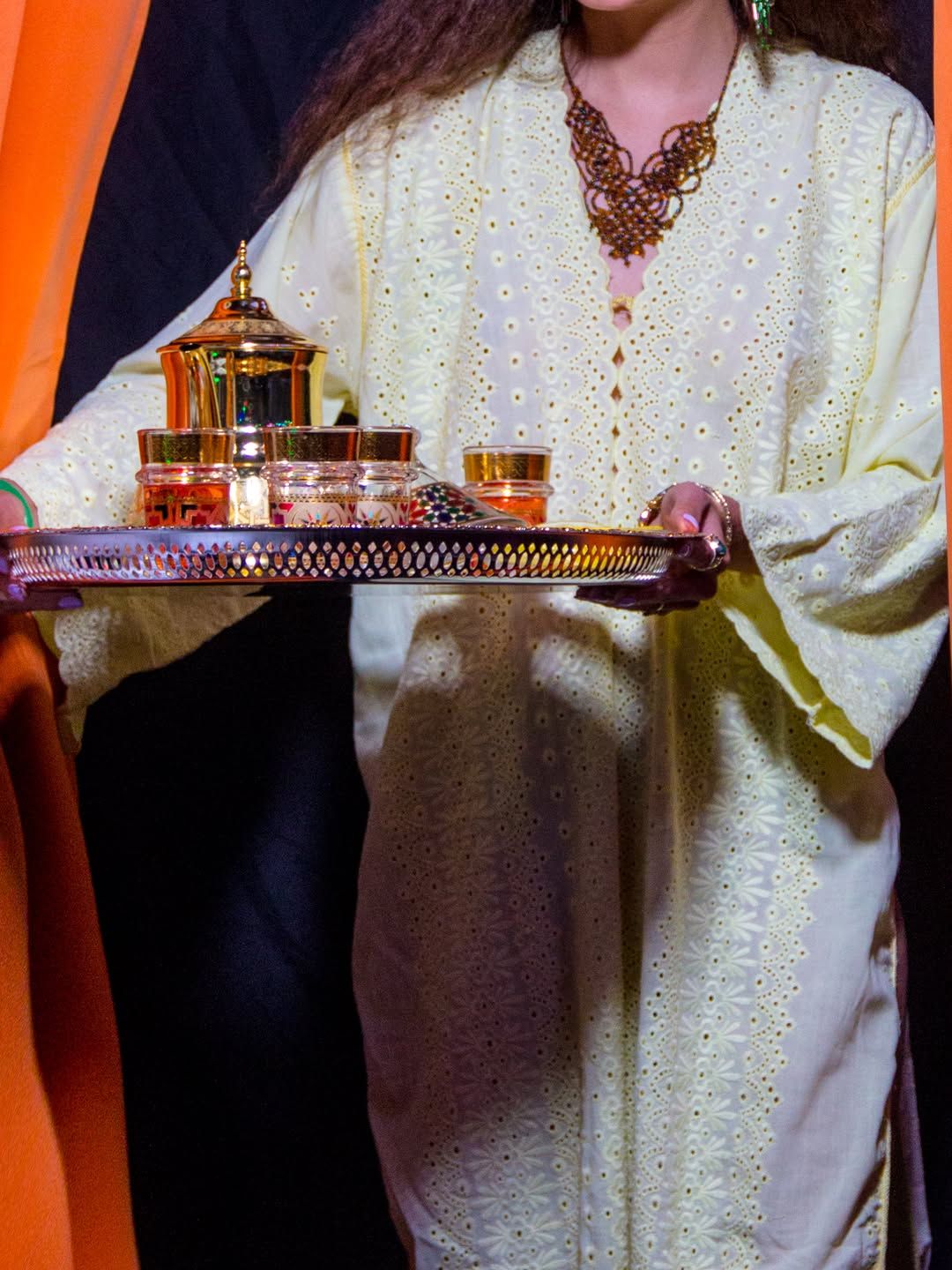 Chef Basmah in a white embroidered kaftan carrying a silver tea tray.