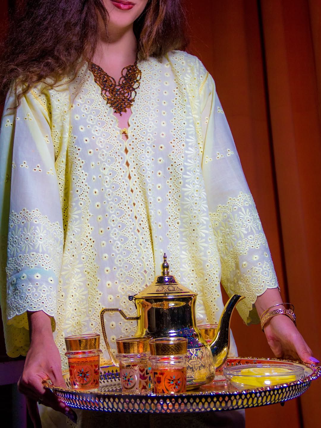 Chef Basmah holding a silver tray with a teapot and tea glasses.
